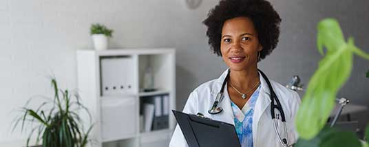 woman physician holds clipboard in office with plants in the background